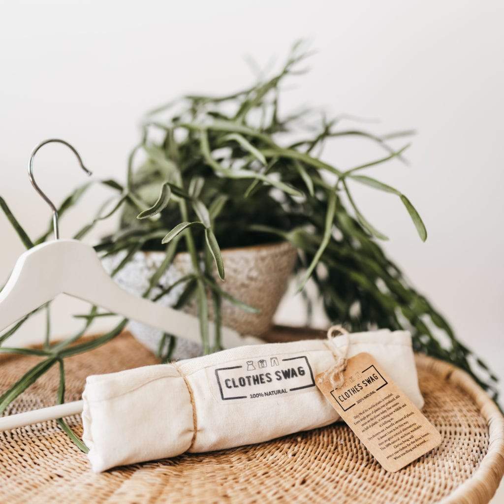 The Clothes Swag rolled up, tied with twine and featuring The Swag swing tag.  A lovely plant and coat hanger in the background - The Swag AU